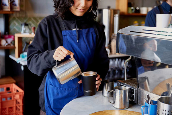 Cafe worker pouring coffee into black Fressko camino coffee cup
