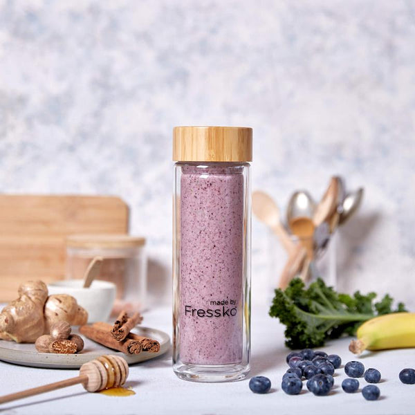 Berry smoothie in Fressko glass flask surrounded by kale berries and honey