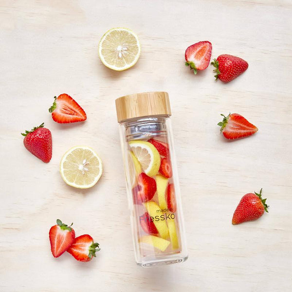 Fruit water inside flass flask surrounded by strawberry and lemon