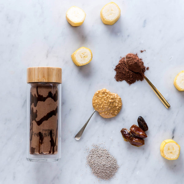 Snickers smoothie in glass fressko flask surrounded by ingredients
