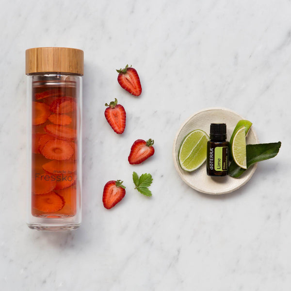 Glass fressko flask with fruit water surrounded by strawberries and lime